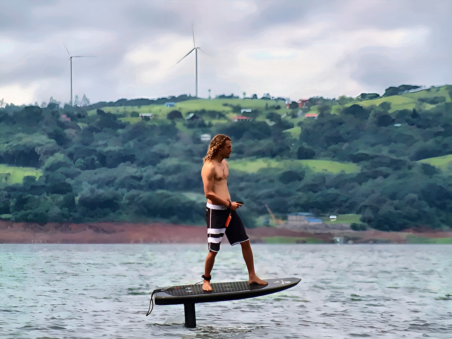 Rider volando en eFoil con las turbinas eólicas del Lago Arenal al fondo